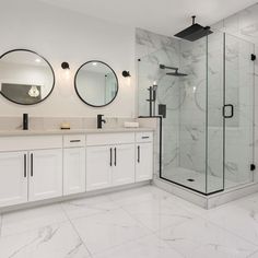 a white bathroom with marble flooring and two round mirrors on the wall above the sinks