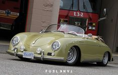 an old green sports car parked in front of a firetruck with the number 533 on it