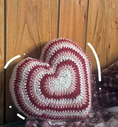 a crocheted heart sitting on top of a bed next to a wooden wall