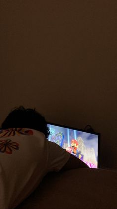 a person laying in bed with their head on the pillow while watching cartoons on tv