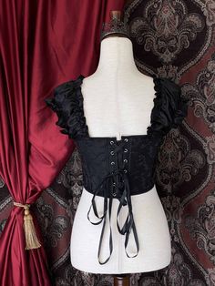 A corset as rich as caviar, this modern take on a classic design incorporates stretchy gathered ruffle sleeves as the straps, adjustable size back corset-lacing, a convenient side zip, and beautifully embroidered black fabric. The perfect corset for any historical fashion enthusiast looking to embody the luxe look of a duchess! Sizing: ✧IN✧ Bust Waist S 30-34 Inches 24-28 Inches M 34-38 Inches 28-32 Inches L 38-42 Inches 30-34 Inches XL 40-44 Inches 36-40 Inches ✧CM✧ Bust Waist S 75-85 CM 60-70 Puff Sleeve Fitted Corset Dress For Costume Party, Black Ruched Fitted Bodice Corset, Black Ruched Corset With Fitted Bodice, Elegant Black Ruched Corset, Elegant Fitted Corset Dress With Ruffles, Elegant Underbust Corset With Ruffles, Elegant Overbust Bodice With Ruffles, Ruched Underbust Corset Dress, Fitted Puff Sleeve Corset Dress With Ruffles