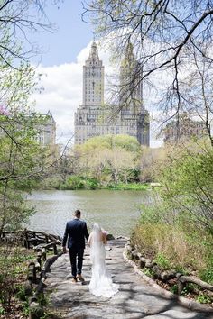 a bride and groom walking down a path by the water in central park