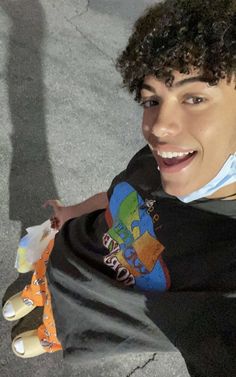 a young man with curly hair is smiling and holding his skateboard in one hand