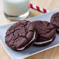 three chocolate cookies with white frosting on a plate next to a glass of milk