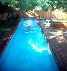 two people are swimming in a pool surrounded by wooden decking and fenced area