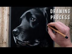 a person is drawing a black dog on a piece of wood with a pencil in their hand