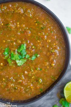 a black bowl filled with soup and garnished with cilantro, parsley and lime