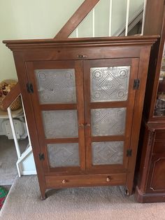 an old wooden cabinet with glass doors in the corner next to a dresser and stairs