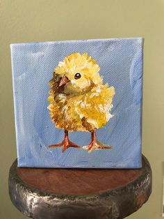 a painting of a yellow chick on a blue background is sitting on a wooden table