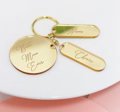 two personalized gold - plated keychains with names on them sitting on a white plate