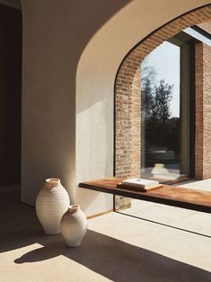 two white vases sitting on top of a wooden table next to a brick wall