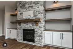 an empty living room with white cabinets and a stone fireplace in the center, surrounded by built - in shelving