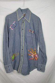 "This vintage 1970s Mr Cellini men's long sleeve chambray shirt was enhanced with fun embroidered accents, front and back. Although it was officially made for a man, its former female owner has given it a definite feminine look with her handiwork. The embroidery at the front features a mouse with cheese, a colorful floral print fabric hand applique,  a butterfly and the initials CZ above the lapel pocket. The backside features a large embroidered bird cage!  The trim at the collar and down the f Retro Embroidered Shirt For Spring, Vintage Embroidered Fall Shirt, Vintage Embroidered Spring Shirt, Retro Embroidered Cotton Shirt, Hippie Long Sleeve Cotton Shirt, Pointy Collar, Embroidered Bird, Floral Print Fabric, Hand Applique