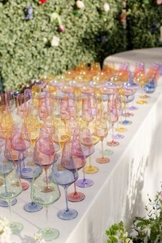 many wine glasses are lined up on a table with flowers in the backround