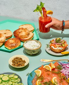 a table topped with plates of food and drinks next to bread, cucumbers, pickles, and other foods