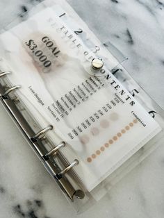 a close up of a note book on a marble surface with metal clippings