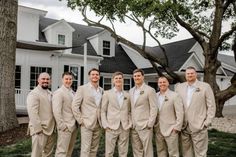 a group of men standing next to each other in front of a white house with trees