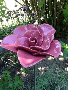 a large pink flower sitting on top of a metal pole in front of some plants