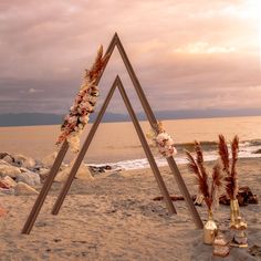 an artistic display on the beach with flowers and feathers in front of it at sunset