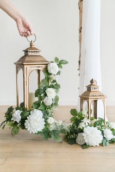 two gold lanterns with white flowers and greenery on the floor next to each other