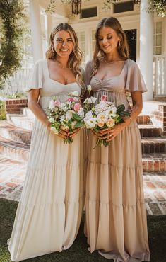 two women standing next to each other in front of a house holding bouquets of flowers