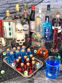 a table topped with bottles and glasses filled with liquid next to a skull head statue