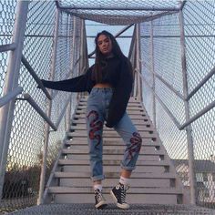 a woman standing on top of a set of stairs wearing ripped jeans and black sweater