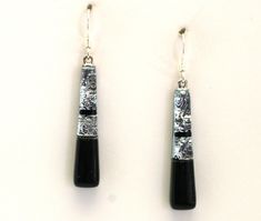 two black and silver earrings on a white surface with one dangling from the earring