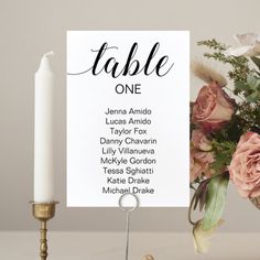 a table number sign with flowers and candles on it next to a white candle holder