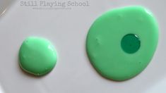 two green buttons sitting on top of a white plate next to each other in front of the words still playing school