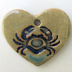 a heart shaped ceramic pendant with a crab on it's side and an eye in the center