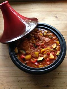 a bowl filled with food sitting on top of a wooden table next to a red vase