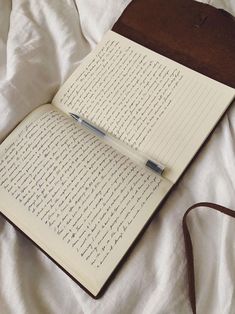 an open book with writing on it sitting on a bed next to a brown bag