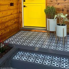 a yellow front door with two planters on the steps and a black and white tiled floor