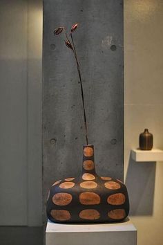 a vase sitting on top of a white pedestal in front of a wall with dots