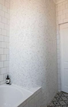 a white bath tub sitting under a window next to a tiled floor and wall in a bathroom