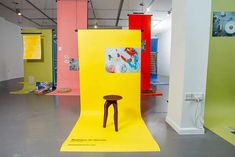 an art gallery with various colored walls and furniture in it's display area, including a yellow chair