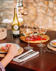 a person sitting at a table with food and wine in front of them on plates