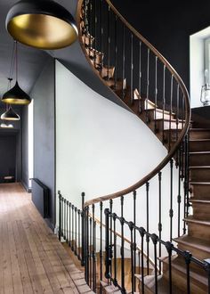 a spiral staircase in a house with black walls and wooden floors, two lamps hanging from the ceiling