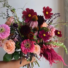 a woman holding a bouquet of flowers in her hand with pink, red and purple colors