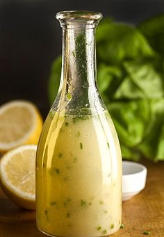 a glass bottle filled with dressing next to lemons and spinach