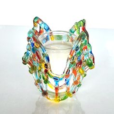 a glass vase filled with lots of different colored beads on top of a white table