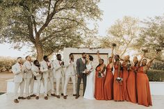 a group of people standing next to each other in front of a tree with their hands up