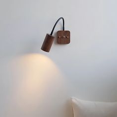 a wall mounted lamp on the side of a white wall next to a brown pillow