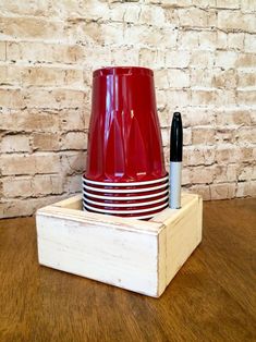 a stack of red cups sitting on top of a wooden box next to a pen