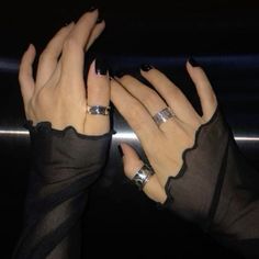 two hands with rings on their fingers in front of a black background, one holding the other's hand