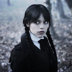 a woman with black hair and braids standing in the woods looking at the camera