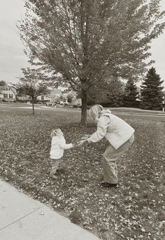 a woman holding the hand of a small child in front of a tree on a field