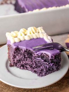 a slice of purple cake with white frosting on a plate next to a fork