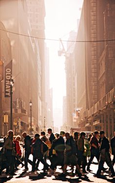 a group of people walking across a street next to tall buildings on a sunny day